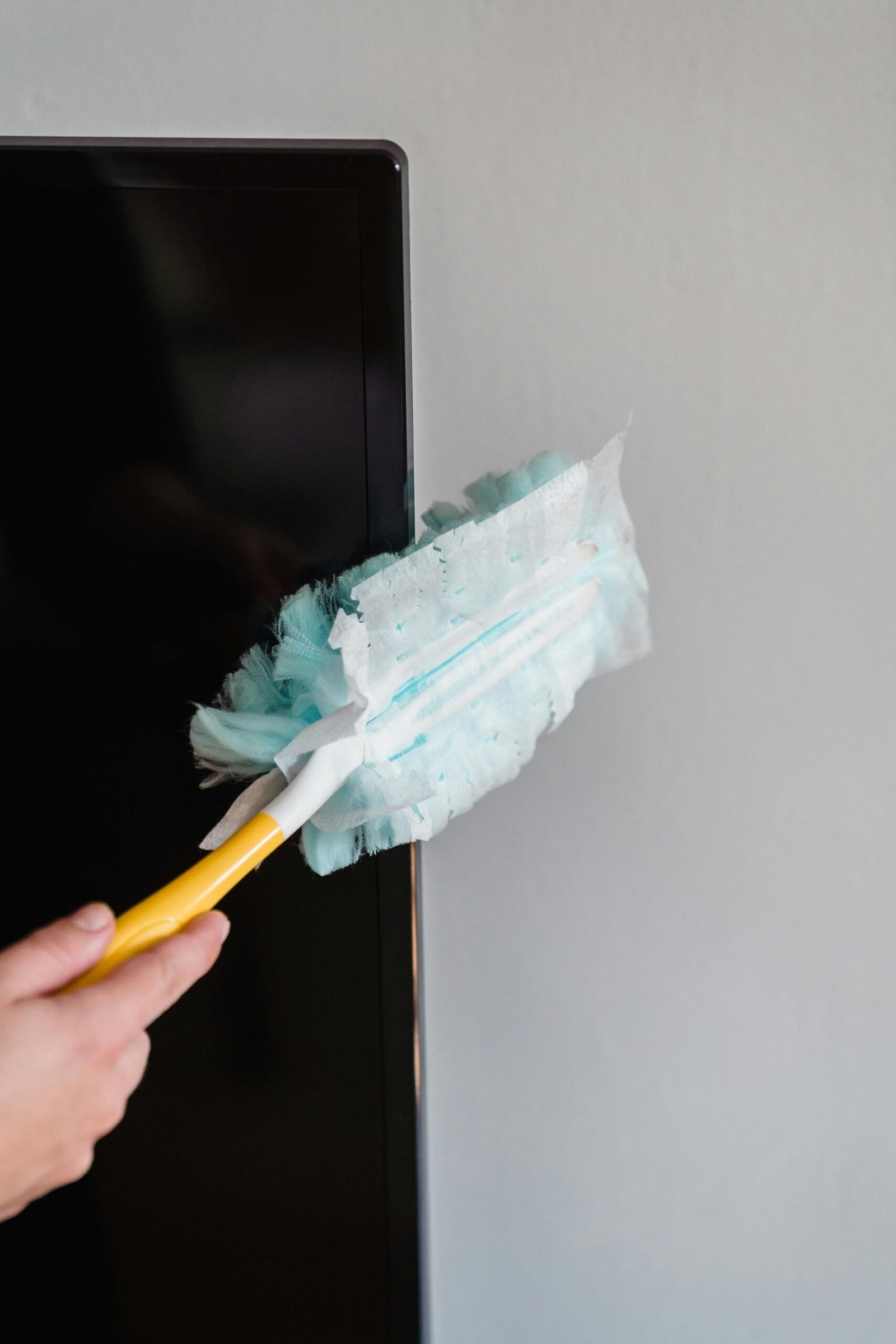 Close-up of a hand using a feather duster to clean a TV screen indoors.